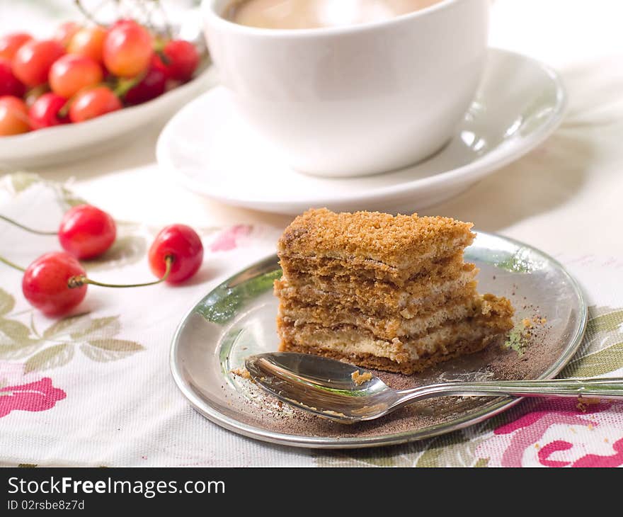 Slice of honey cake on a plate with spoon and coffee in background. Slice of honey cake on a plate with spoon and coffee in background.