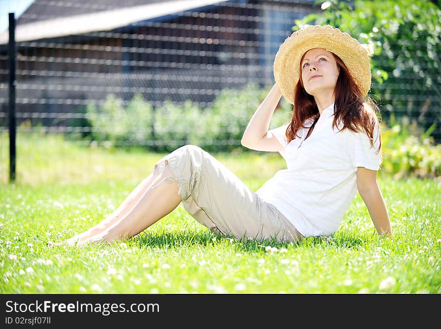 Young woman in straw hat  sitting on green grass