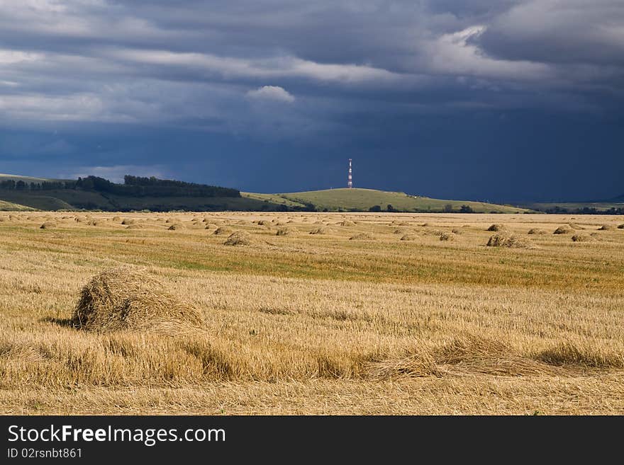 The heavy dirty thunder-storm storms over a field with hay and stacks. The heavy dirty thunder-storm storms over a field with hay and stacks