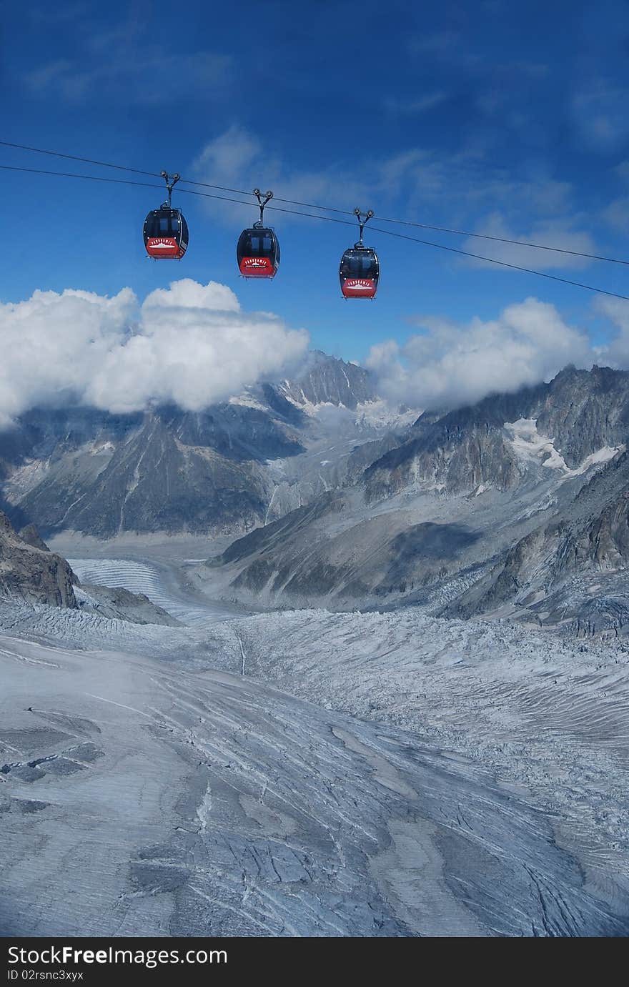 Three red cablecars gliding above the Glacier Blanche near Chamonix and the Aiguille du Midi.