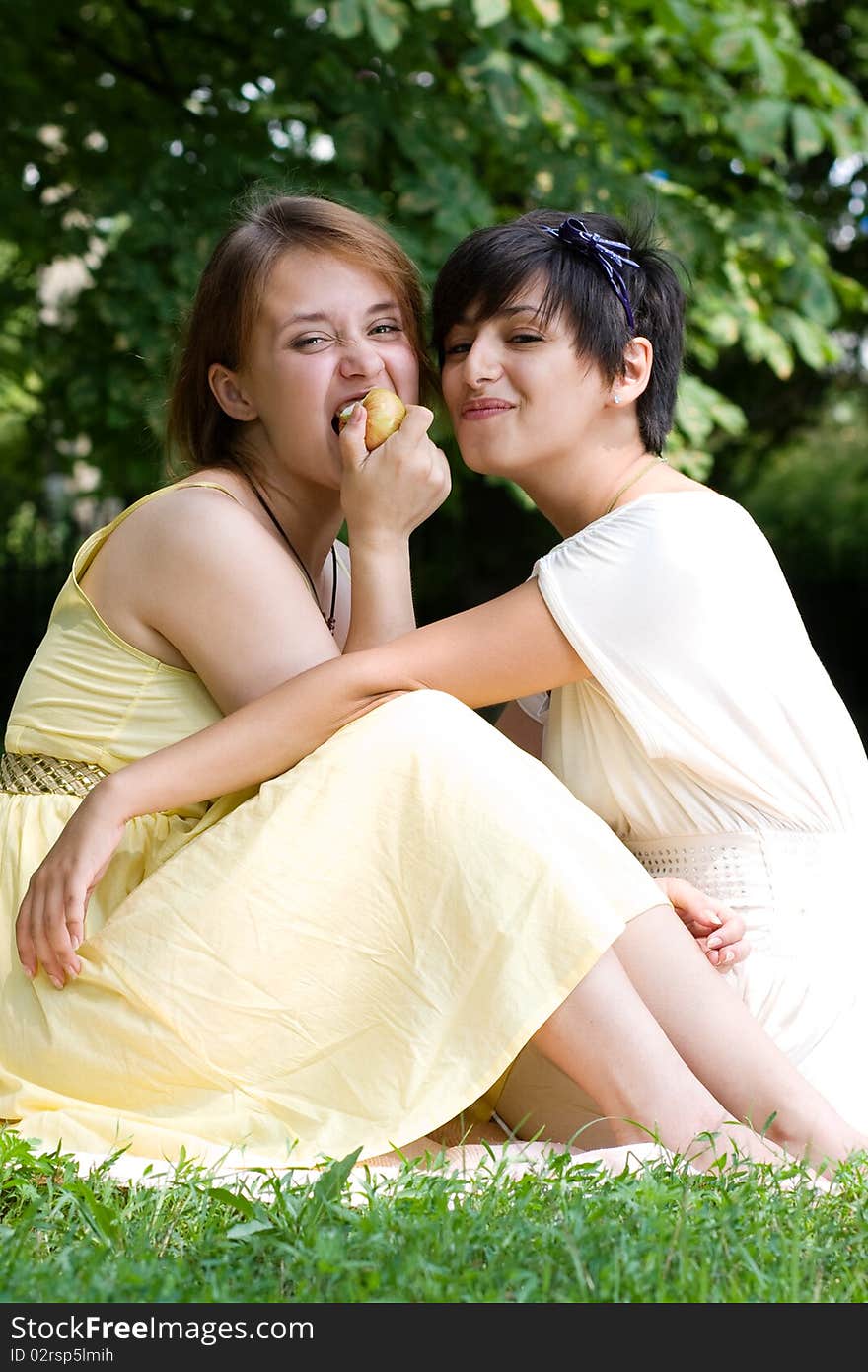 Two Girls Eating An Apple Outdoors Smiling