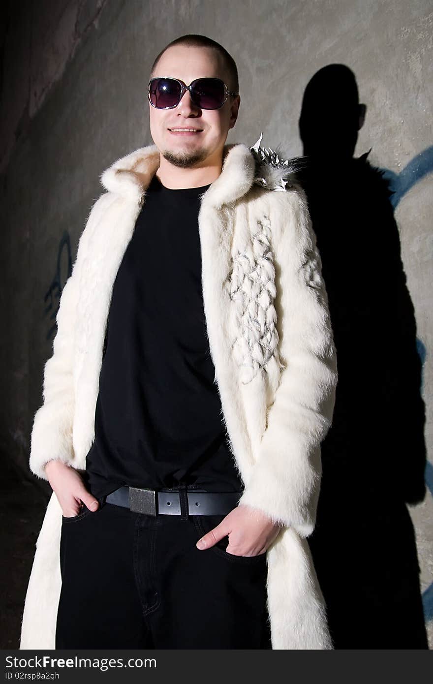 Man in long white chinchilla fur coat posing like a pimp near the grungy wall at night. Man in long white chinchilla fur coat posing like a pimp near the grungy wall at night