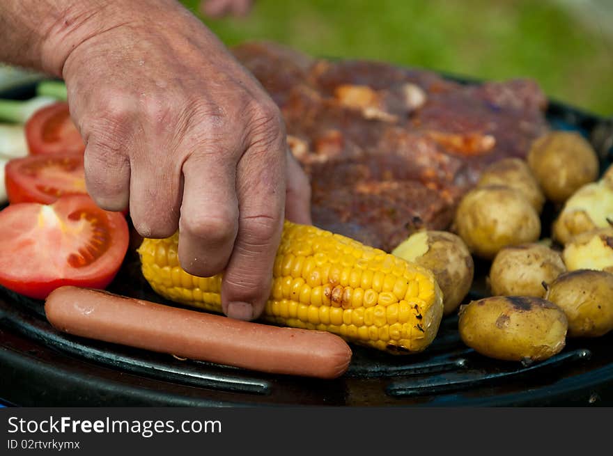 Hand turning a yellow corn on the grill. Hand turning a yellow corn on the grill