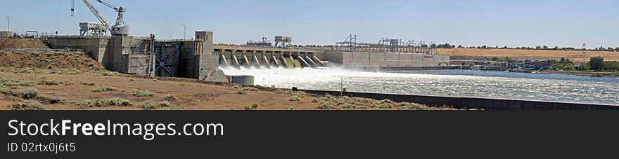 Wide panorama of a concrete dam, with water flowing over the spillway. Wide panorama of a concrete dam, with water flowing over the spillway