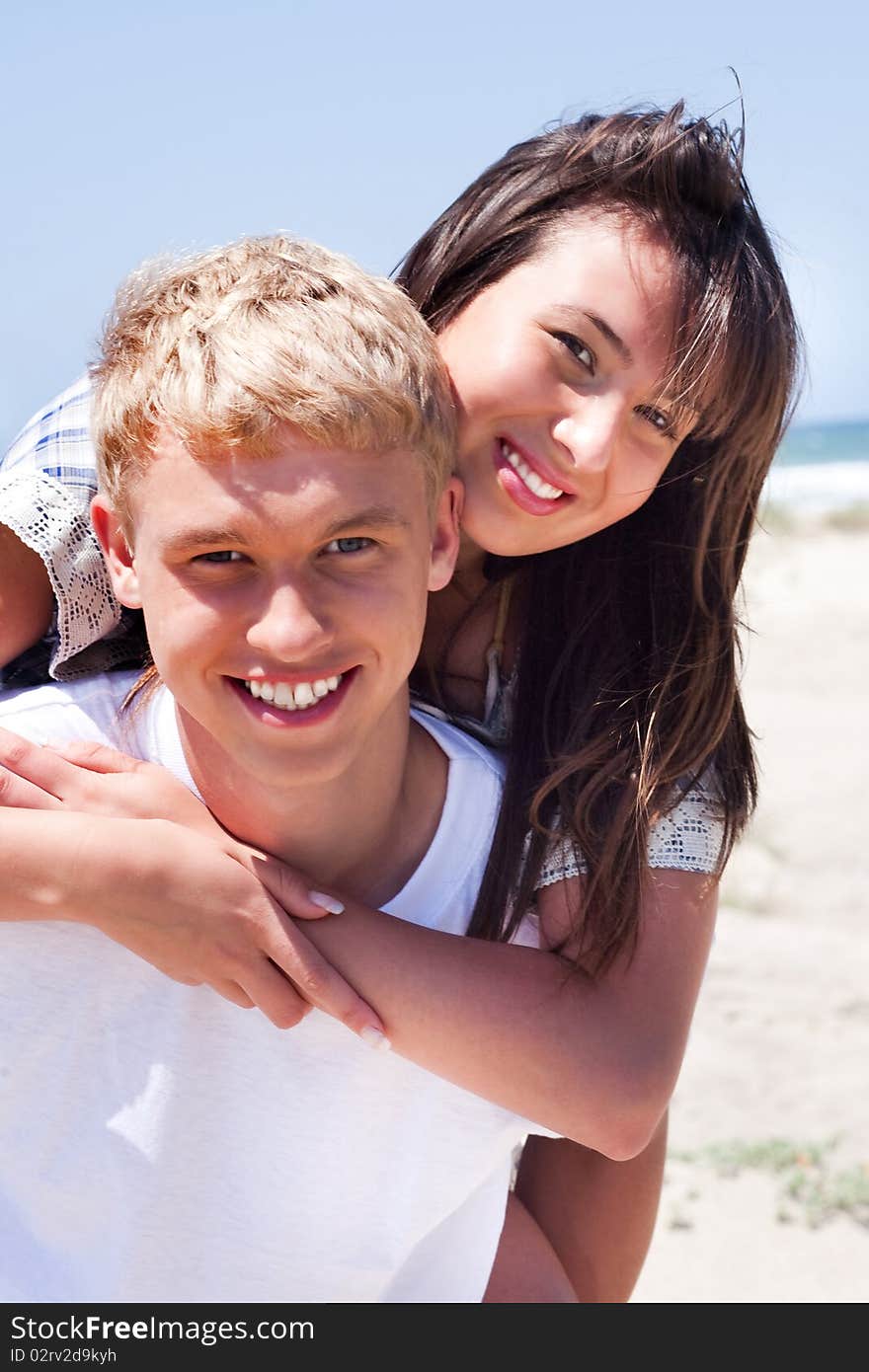 Girl riding on guy at beach and smiling at camera