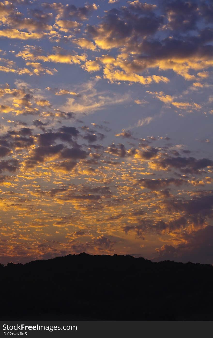 The sky in clouds during a sunset. A vertical shot. There is a silhouette of mountains in the bottom part of a shot.