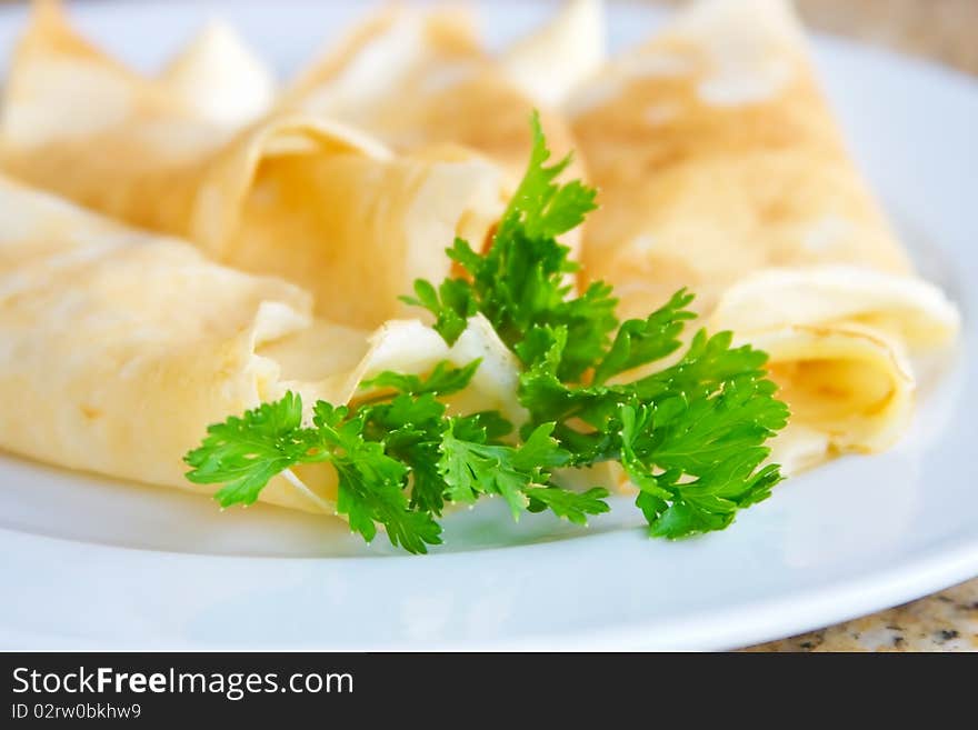 Stuffed pancakes decorated with parsley on a white plate