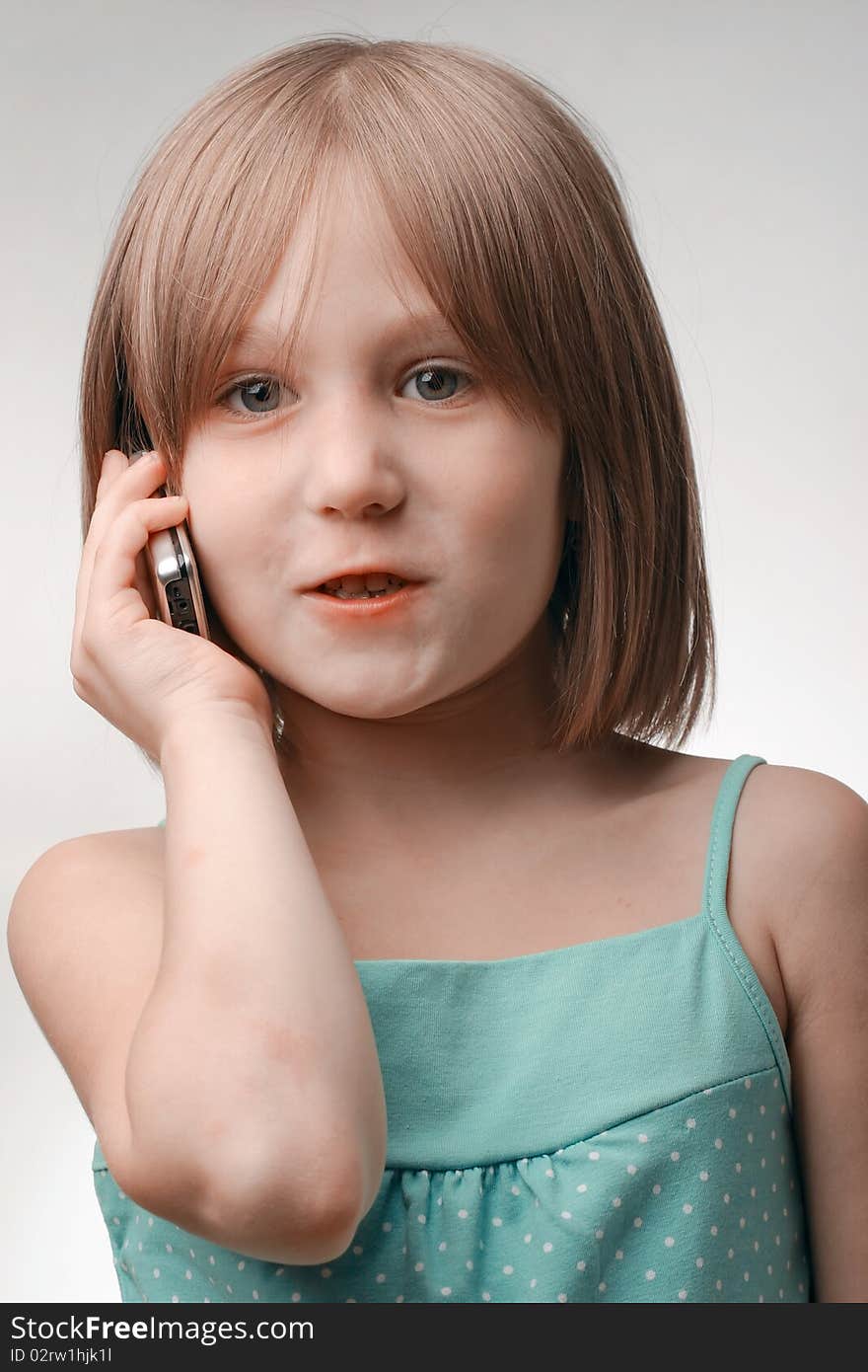 The girl calls by phone. Age of the girl of 5 years. Phone modern, cellular, with the metal case. A background neutral, gray