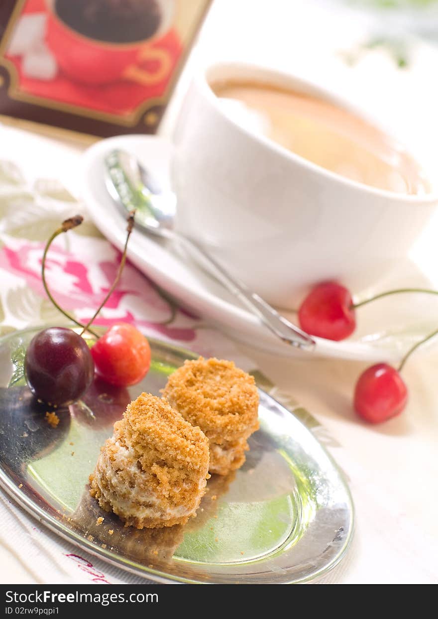 Two small honey cakes on a plate with cherry and coffee in background. Two small honey cakes on a plate with cherry and coffee in background.