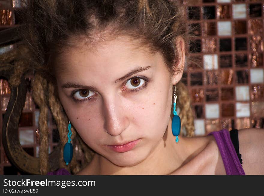 Portrait of a young girl with dreadlocks on the background of a decorative mosaic. big eyes. blue earrings. Portrait of a young girl with dreadlocks on the background of a decorative mosaic. big eyes. blue earrings.