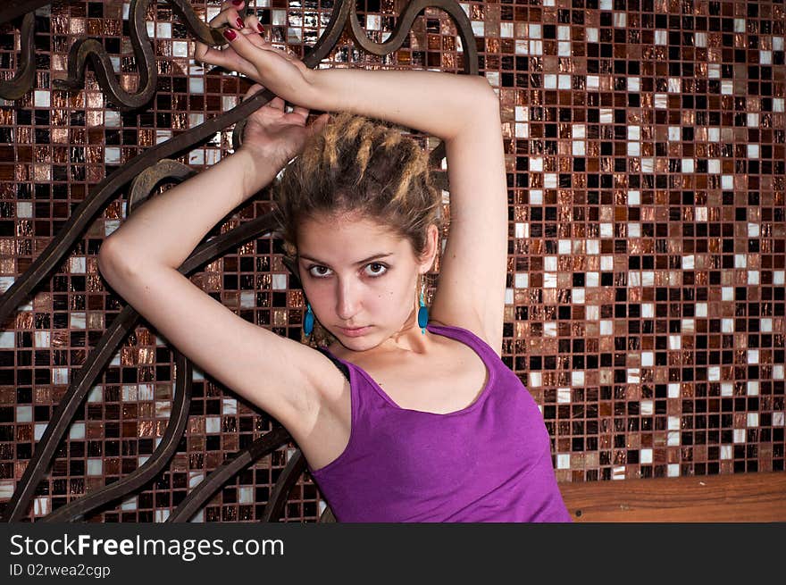 Portrait of a young girl with dreadlocks on the background of a decorative mosaic. big eyes. blue earrings, purple shirt . hands raised. Portrait of a young girl with dreadlocks on the background of a decorative mosaic. big eyes. blue earrings, purple shirt . hands raised.