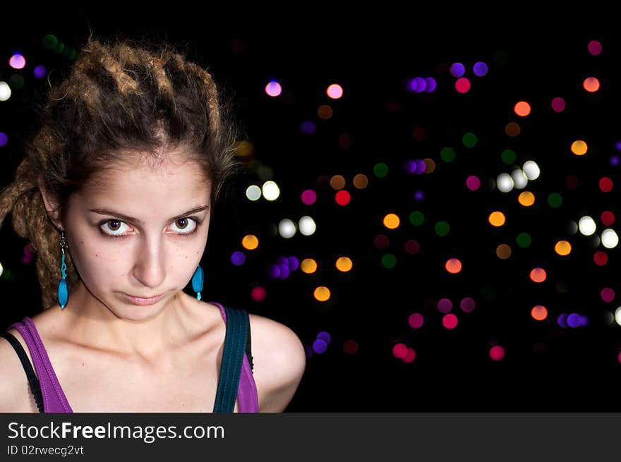 Portrait of attractive young woman on a colorful night lights background.  Big eyes, dreadlocks, blue earrings.