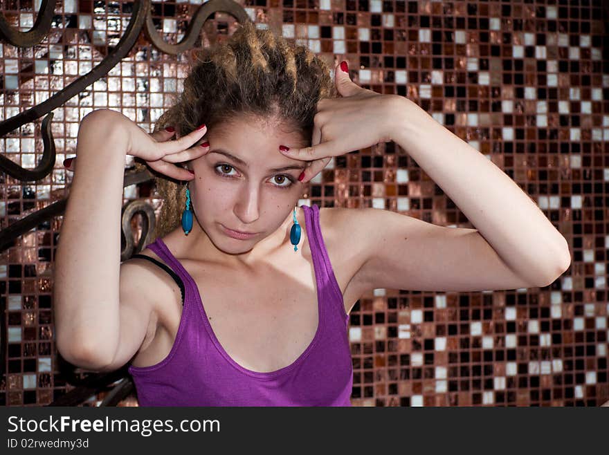 Portrait of a young girl with dreadlocks on the background of a decorative mosaic. big eyes. blue earrings, purple shirt . hands raised. Portrait of a young girl with dreadlocks on the background of a decorative mosaic. big eyes. blue earrings, purple shirt . hands raised.