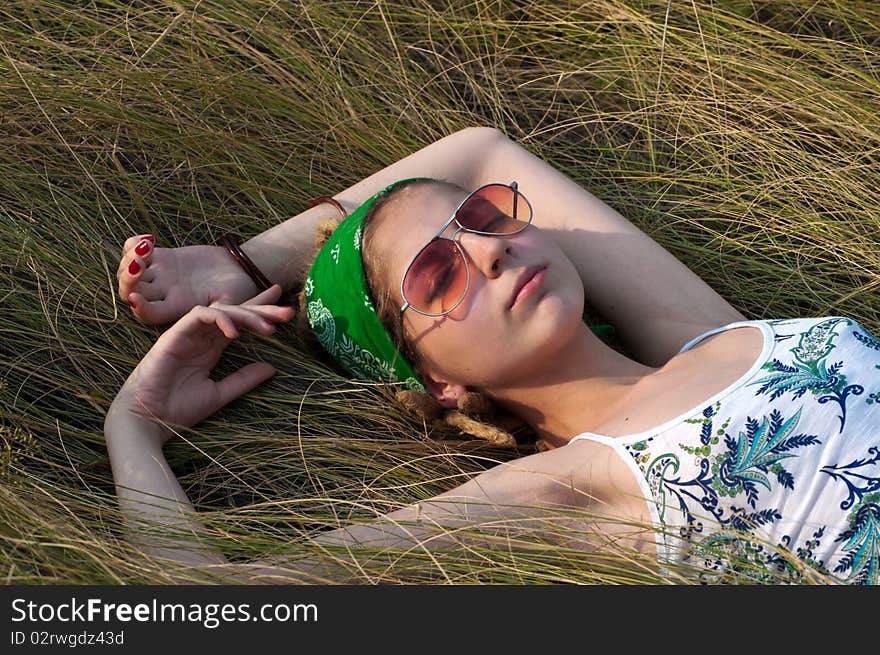 Young woman in a green headscarf and sunglasses lying on the grass. Young woman in a green headscarf and sunglasses lying on the grass