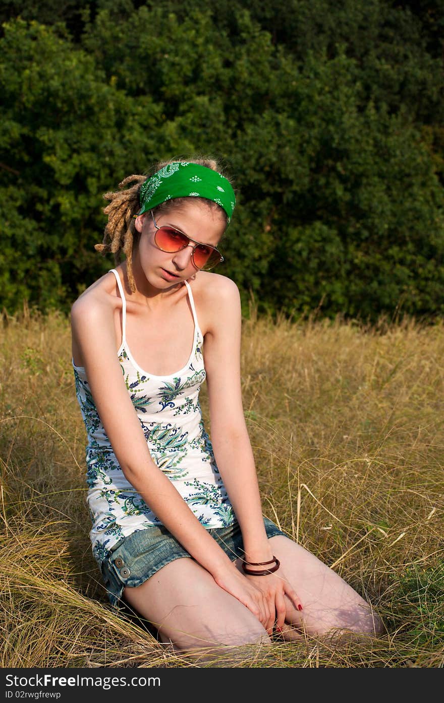 Young woman in a green scarf, sunglasses and a bright  shirt sitting on the grass. Young woman in a green scarf, sunglasses and a bright  shirt sitting on the grass