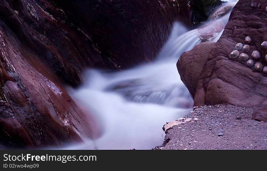 Water cascading between rocks at a beach long exposure. Water cascading between rocks at a beach long exposure