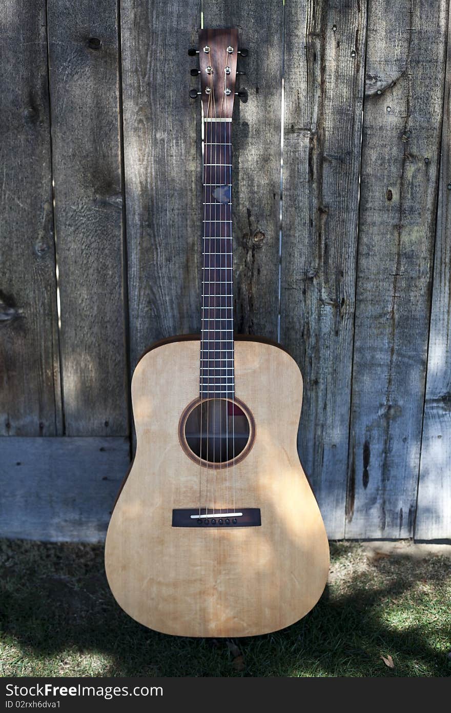 This is a picture of a traditional acoustic custom guitar resting against a fence, sitting on a bed of grass. This is a picture of a traditional acoustic custom guitar resting against a fence, sitting on a bed of grass.