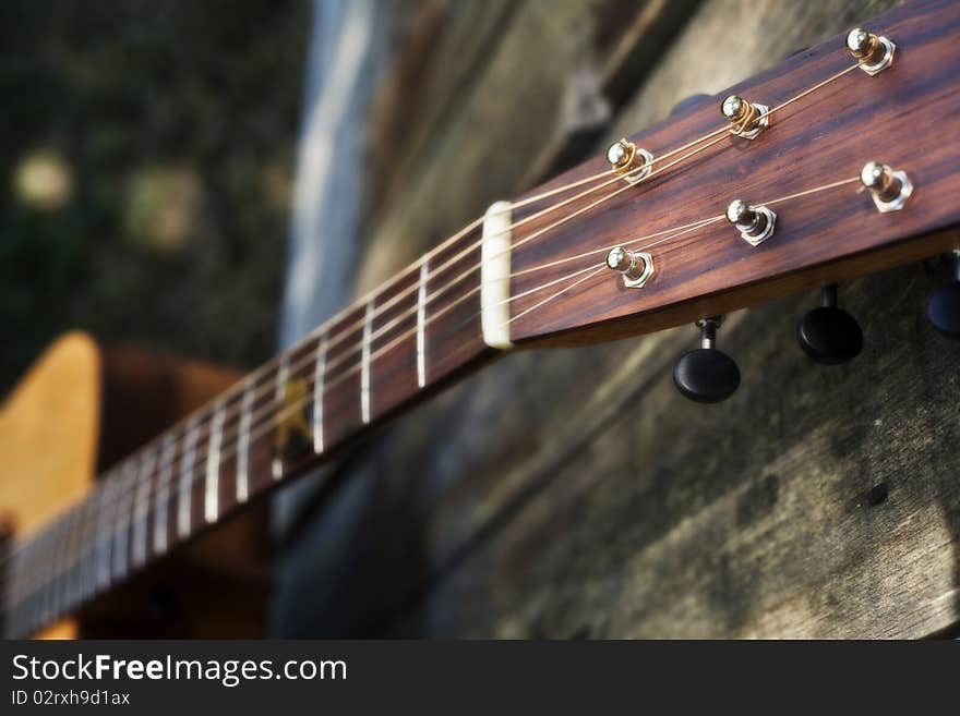 This is a picture of a traditional acoustic custom guitar's fret board resting against a faded fence. This is a picture of a traditional acoustic custom guitar's fret board resting against a faded fence.