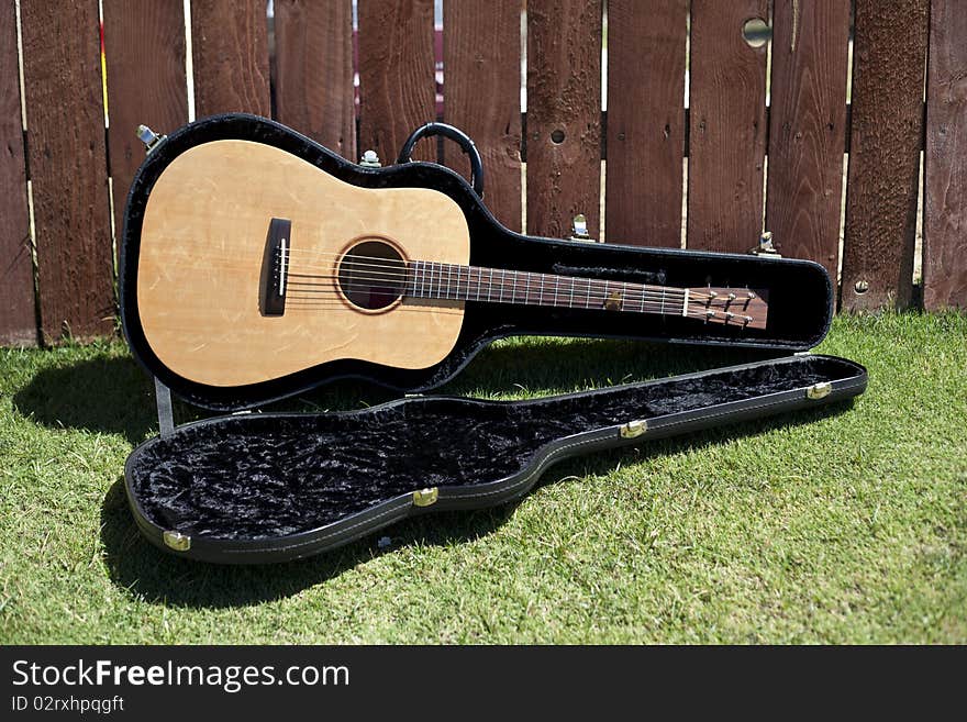 This is a picture of an acoustic guitar in a case against a redwood fence. This is a picture of an acoustic guitar in a case against a redwood fence.