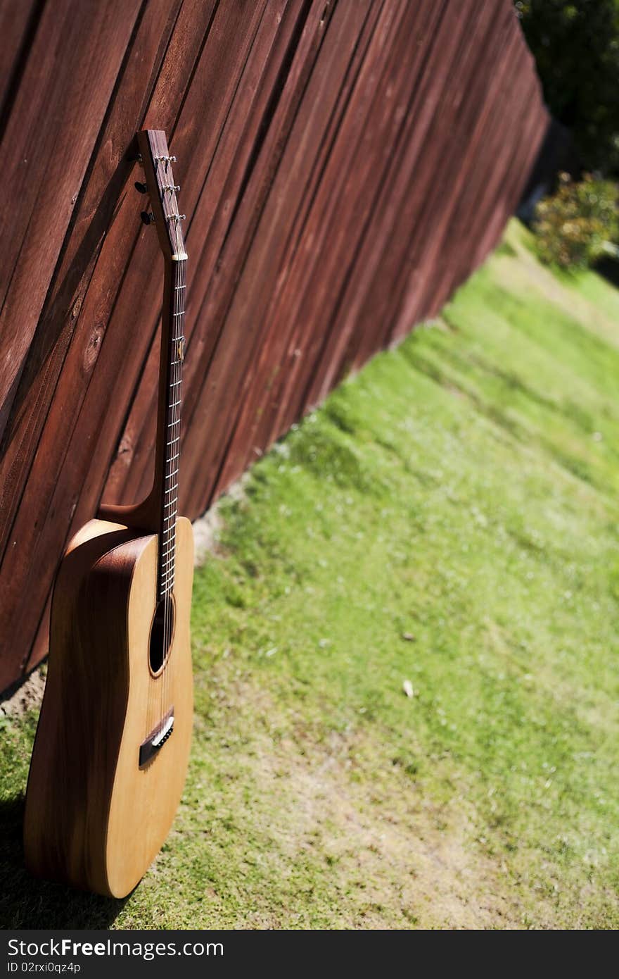 This is a picture of an acoustic guitar against a redwood fence with a long view of the fence. This is a picture of an acoustic guitar against a redwood fence with a long view of the fence..