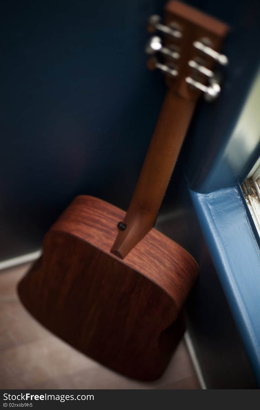 Back view of an acoustic guitar in a corner of a blue wall. Back view of an acoustic guitar in a corner of a blue wall.