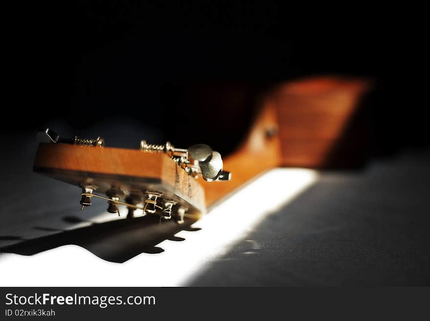 The top/back of a guitar with tuning keys and a slat of light illuminating the neck and keys. The top/back of a guitar with tuning keys and a slat of light illuminating the neck and keys.