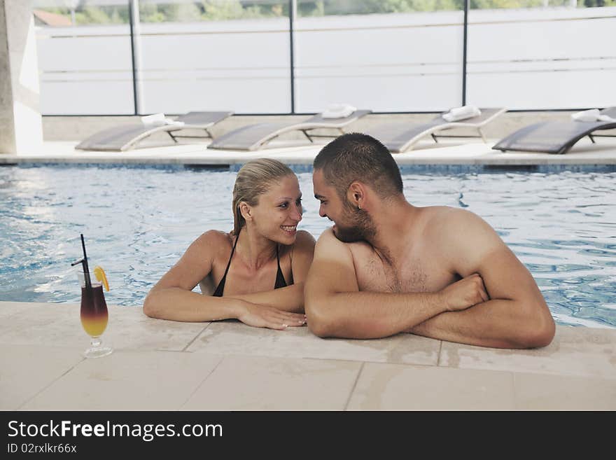 Happy young couple in love have fun  relax and  drink coctail at indoor wellness swimming pool. Happy young couple in love have fun  relax and  drink coctail at indoor wellness swimming pool