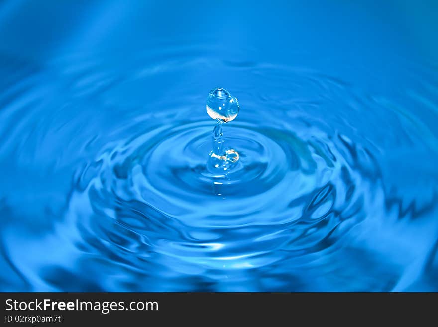 Clean blue drop of water splashing in clear water. Abstract blue background