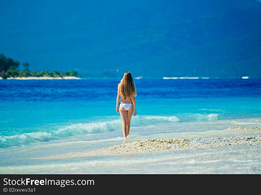 A beautiful woman wearing white bikini facing the sea on a vacant beach in paradise