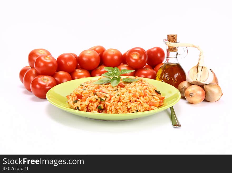 Risotto with tomatoes on a green plate decorated with basil with fresh tomatoes, onions, garlic and olive oil on white background