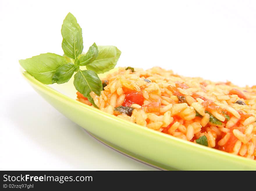 Risotto with tomatoes on a green plate decorated with basil in close up