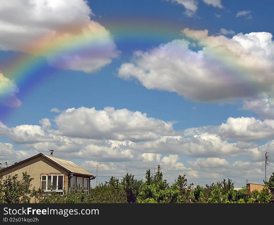 Rainbow and summers cloudy sky above a building and trees