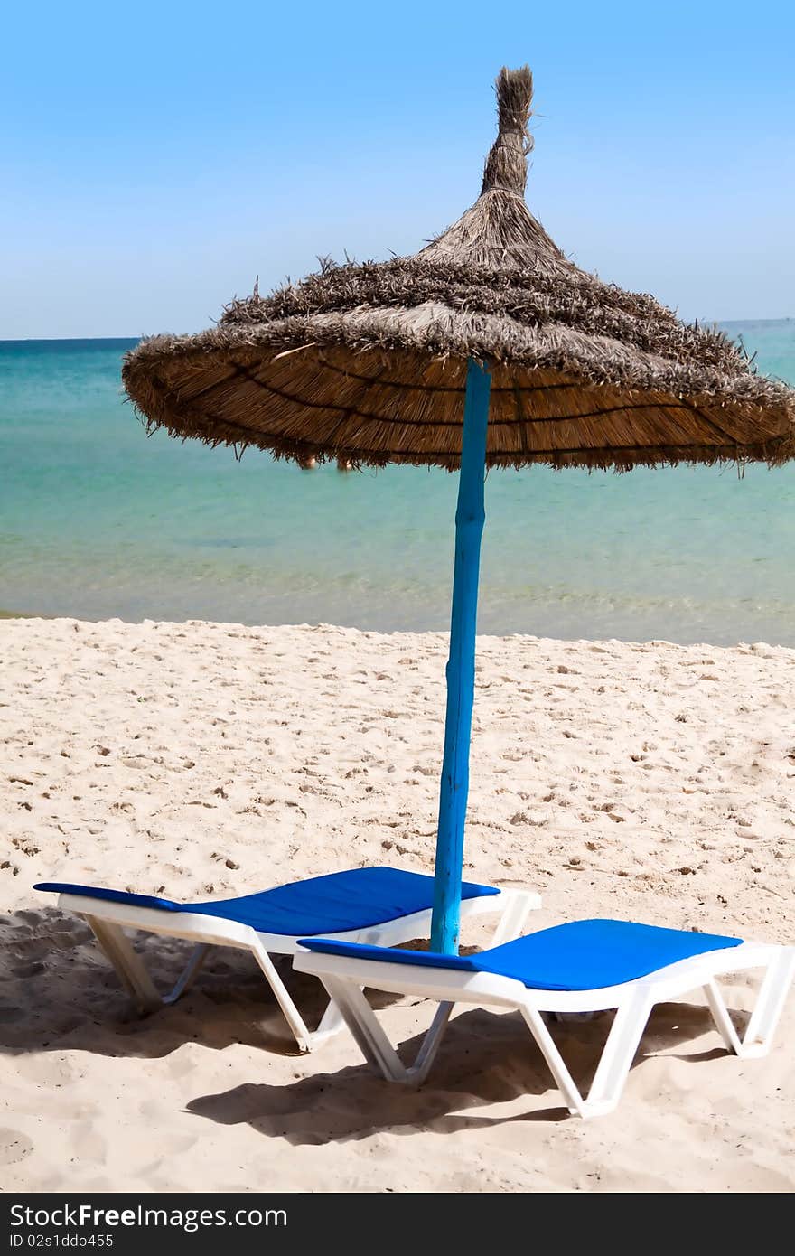 Straw umbrella on the beach with two chairs