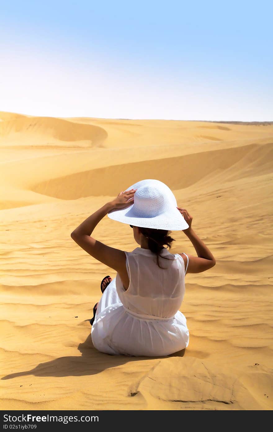 White girl sitting on the desert and putting hat on her head. White girl sitting on the desert and putting hat on her head