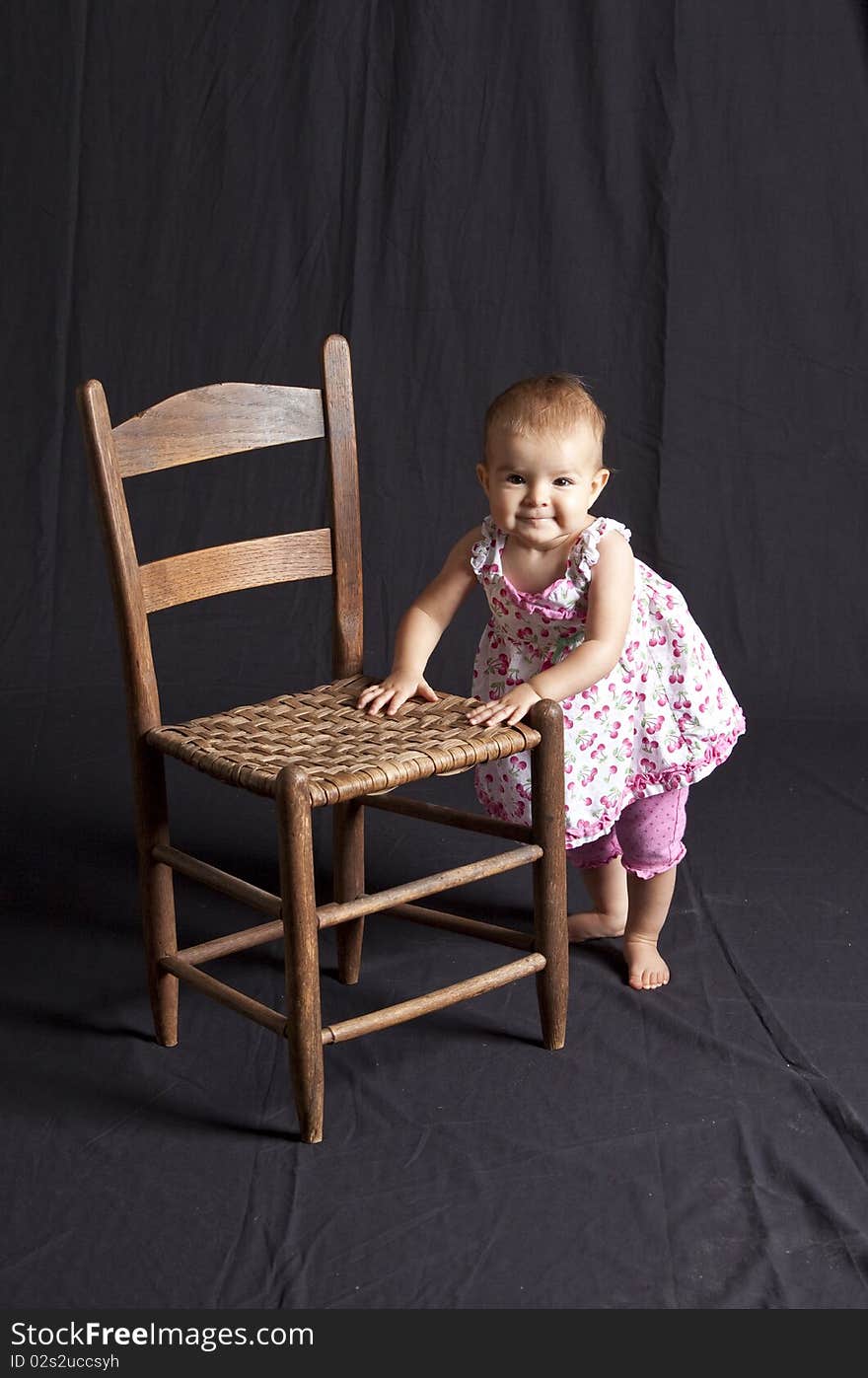 Baby girl posing next to old chair, studio shot. Baby girl posing next to old chair, studio shot