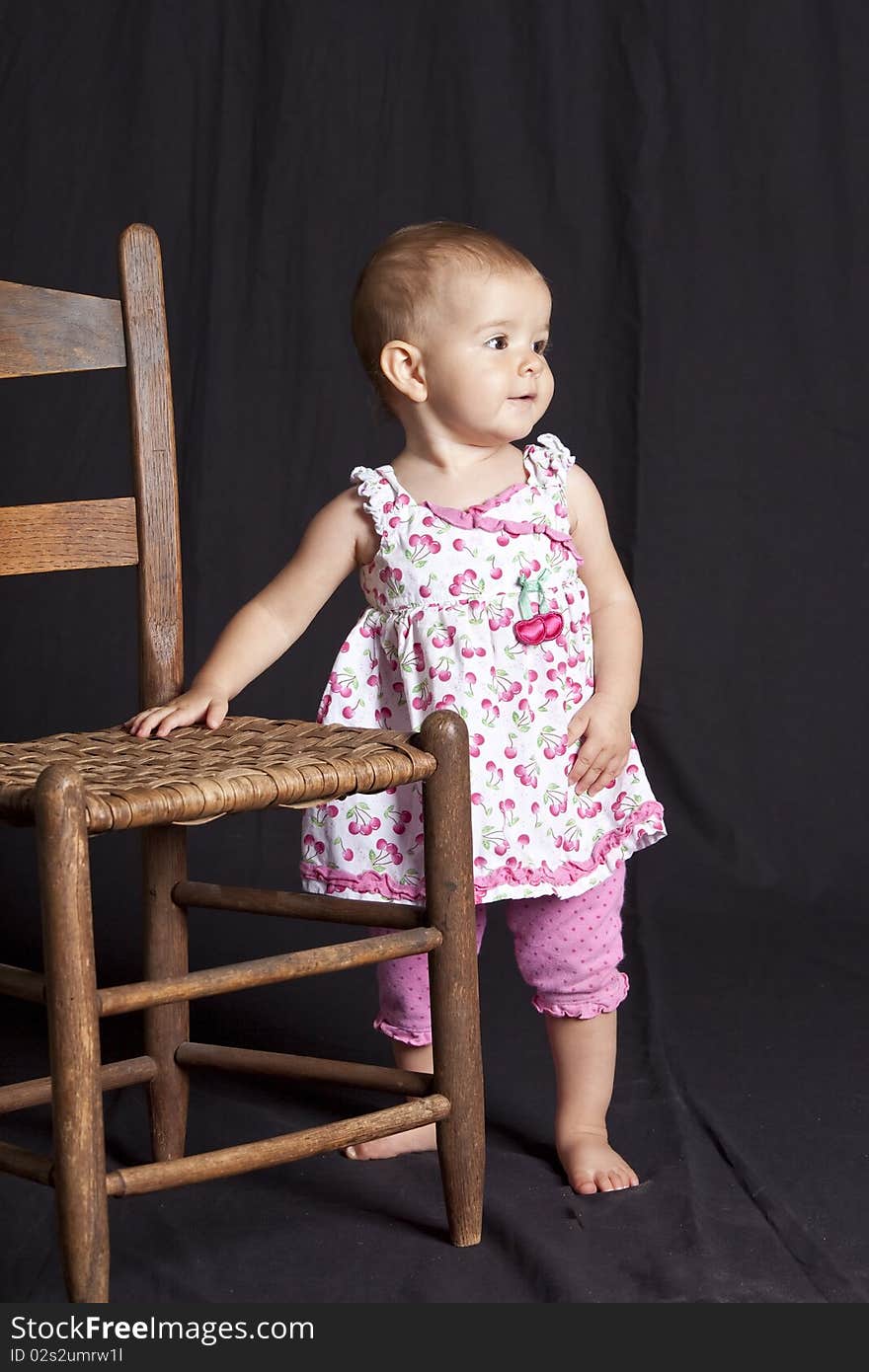 Baby girl posing next to old chair, studio shot. Baby girl posing next to old chair, studio shot