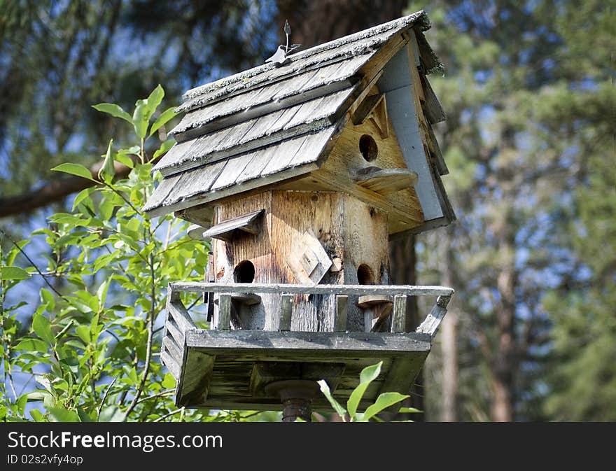 A close-up of a handmade wooden birdhouse with shingled roof and a forest in the background. A close-up of a handmade wooden birdhouse with shingled roof and a forest in the background.