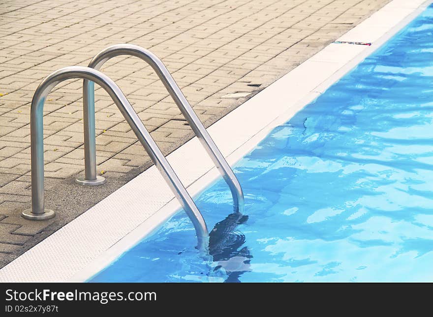 Stainless steel pool ladder goes down into blue water