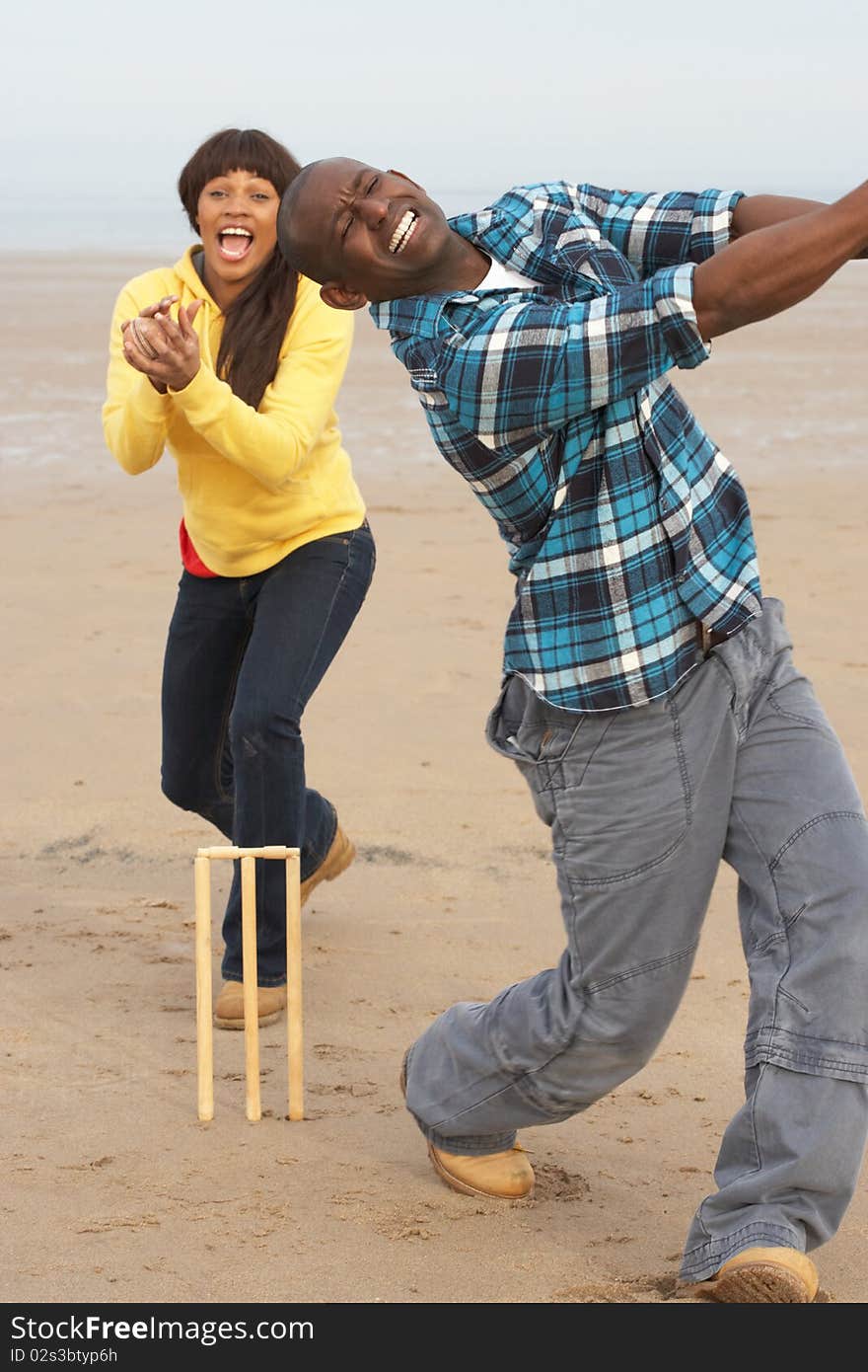 Young Couple Playing Cricket On Autumn Beach Holiday in the sun