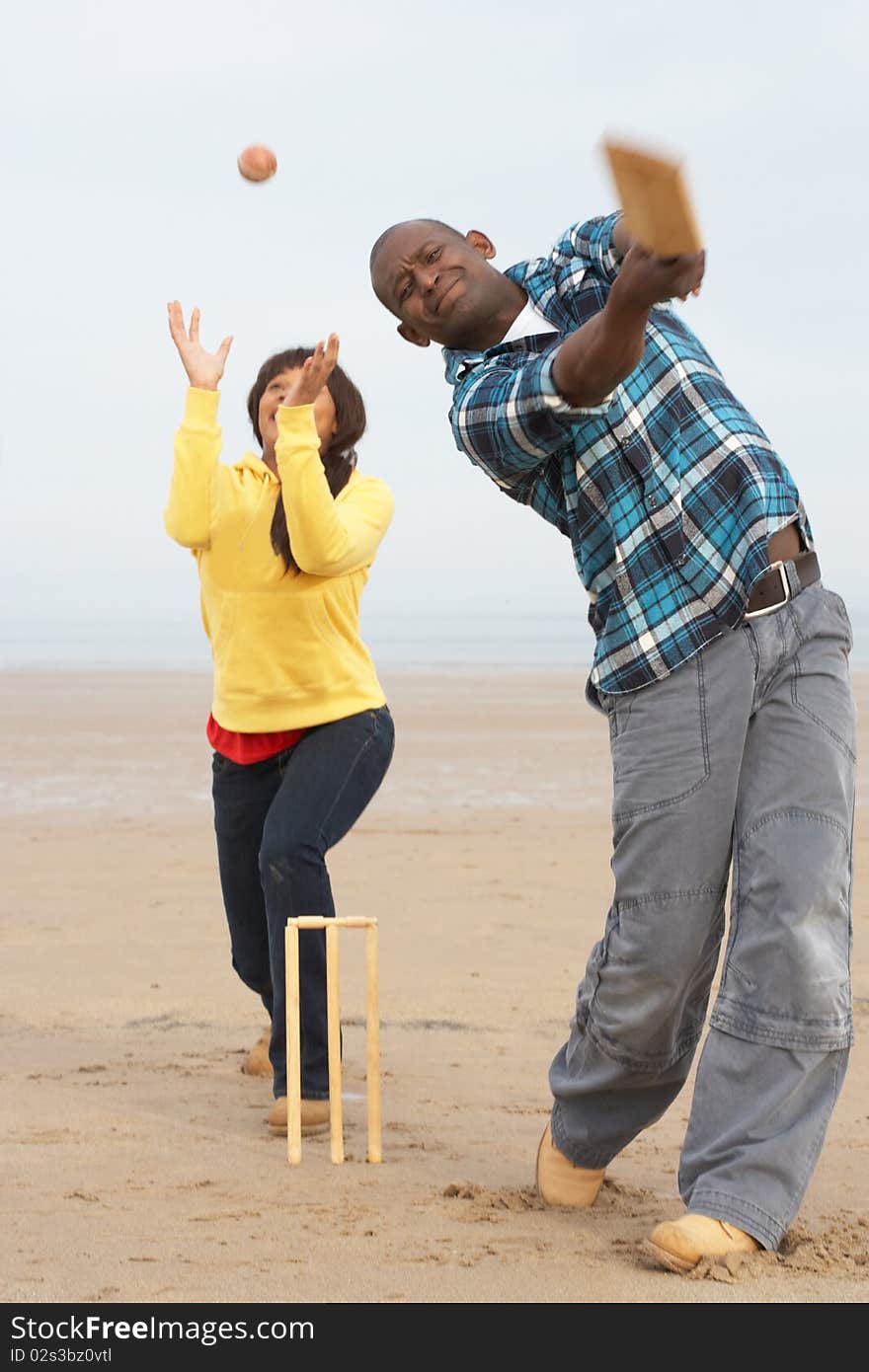 Young Couple Playing Cricket On Beach Holiday