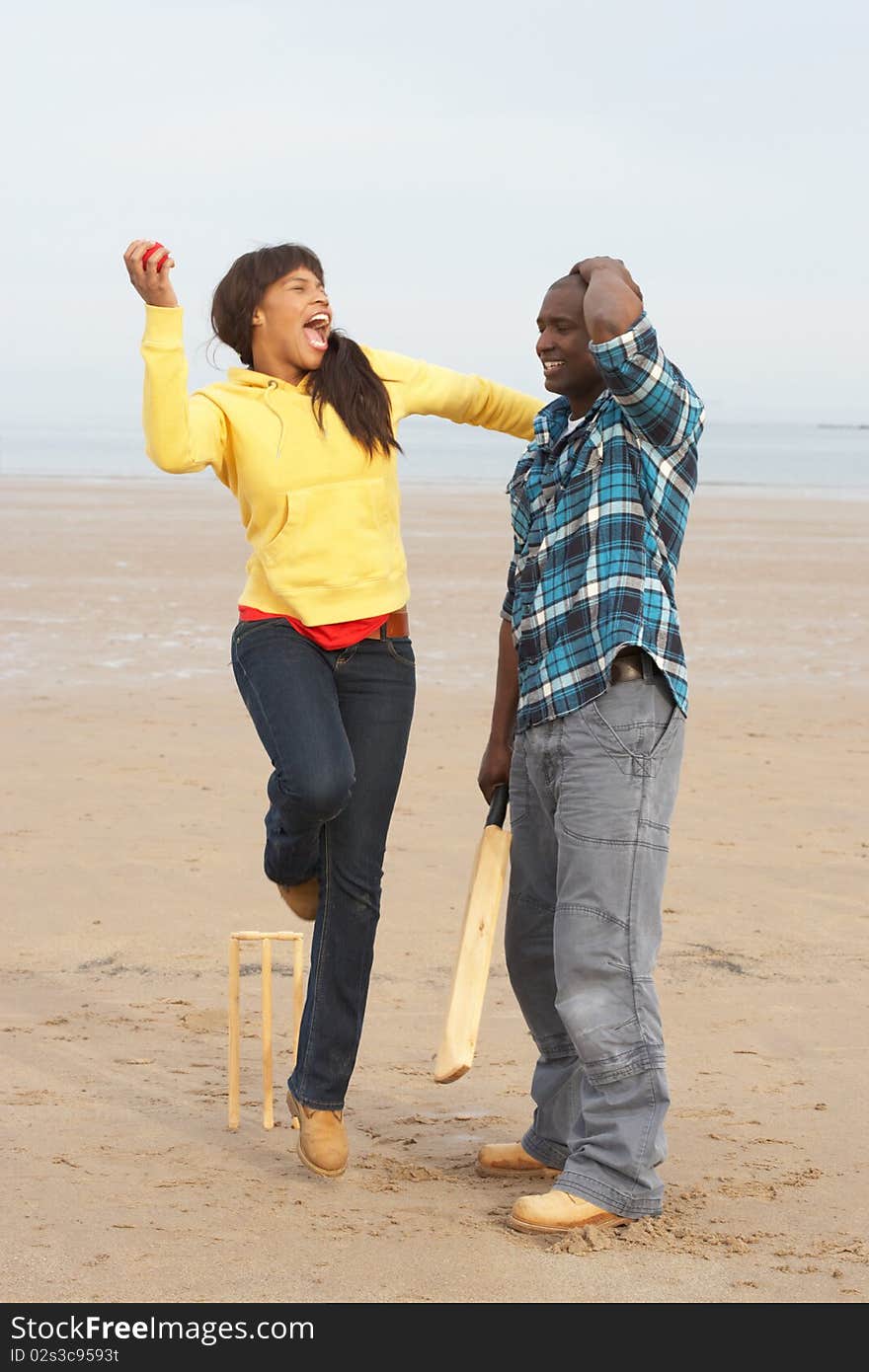 Young Couple Playing Cricket On Beach Holiday