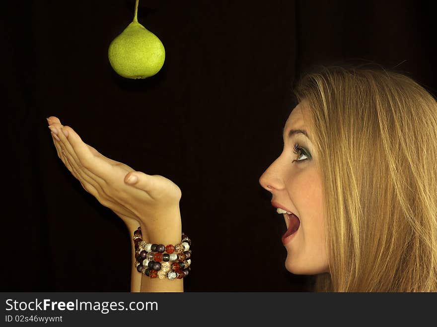 Beautiful girl catches a pear with two hands, isolation on a black background. Beautiful girl catches a pear with two hands, isolation on a black background