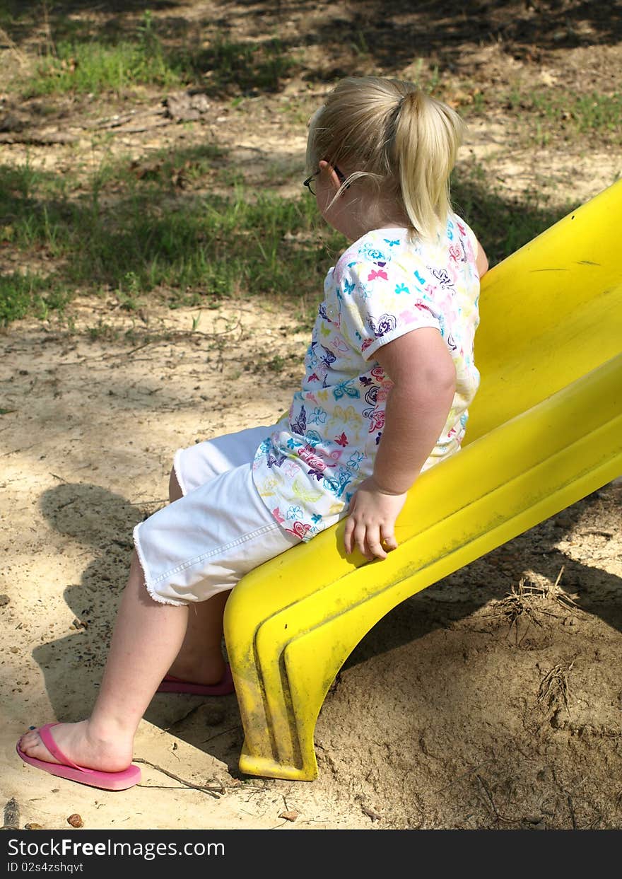 little girl sitting on a yellow slide at playground looking at her own shadow. little girl sitting on a yellow slide at playground looking at her own shadow...