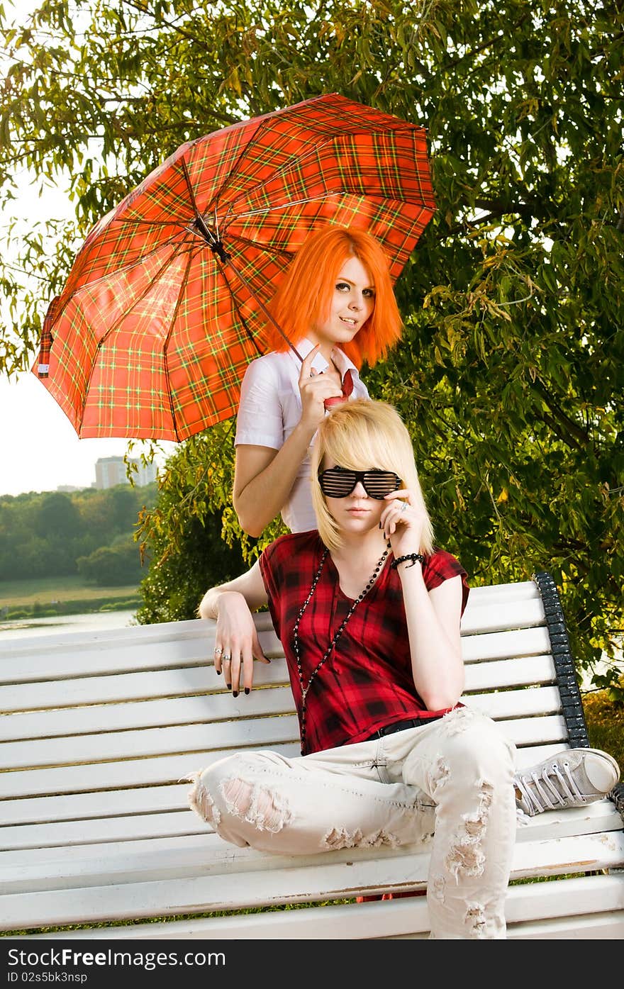 Two teenage girls sitting on a bench at the summer park. Two teenage girls sitting on a bench at the summer park