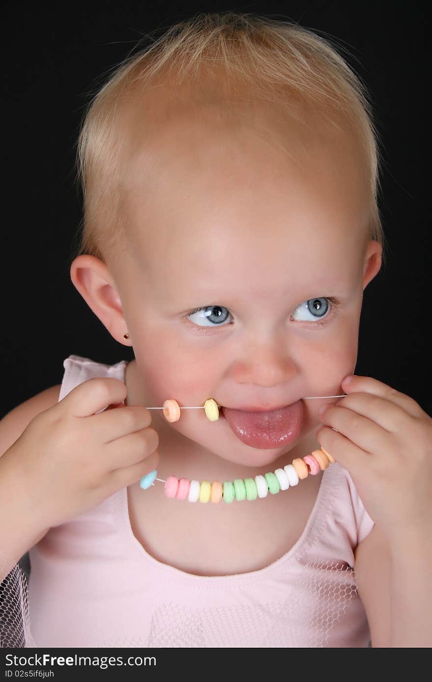 Cute blond baby girl eating a candy necklace. Cute blond baby girl eating a candy necklace