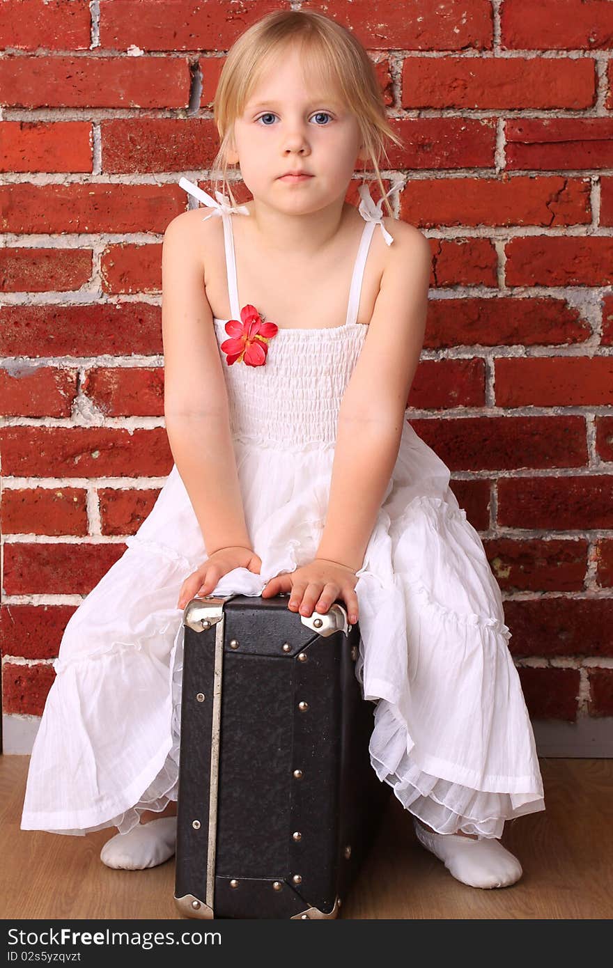 Beautiful little girl sitting on a suitcase. Travel ballet dancer