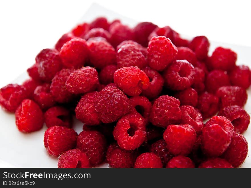 A heap of red raspberries on plate. White background. A heap of red raspberries on plate. White background