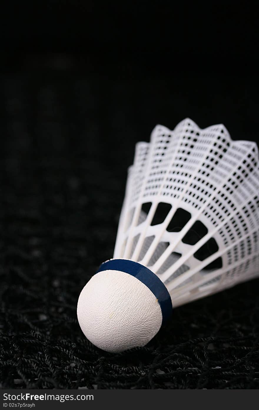 Close-up of a white synthetic shuttlecock on a black badminton net.