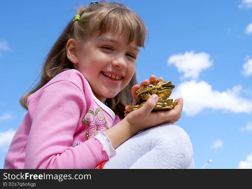 Against the dark blue sky the girl sits laughs, holds in one hand riches symbol - a frog with the Chinese coin, and another irons it. Against the dark blue sky the girl sits laughs, holds in one hand riches symbol - a frog with the Chinese coin, and another irons it