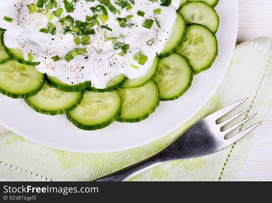 Fresh cucumber slices with sour cream and green onion on a plate